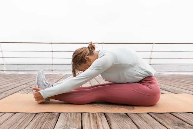 Full shot woman stretching sur tapis de yoga