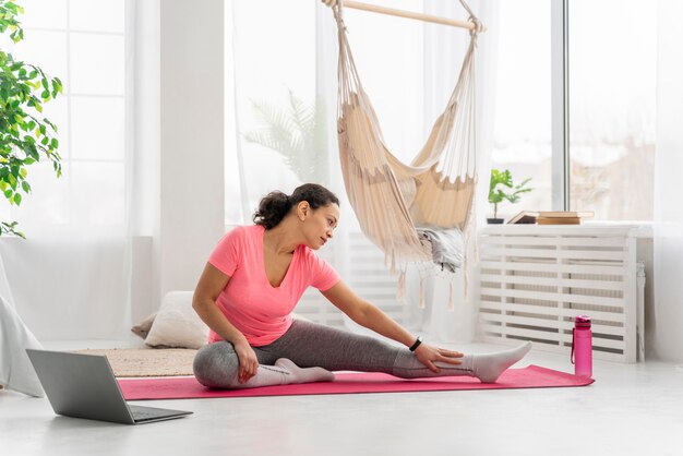 Full shot woman stretching sur tapis