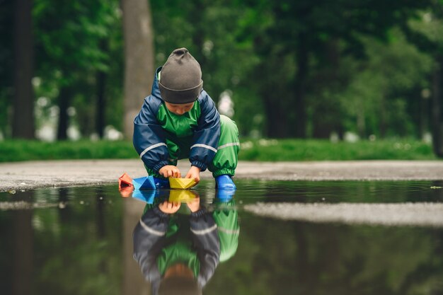 Funny kid en bottes de pluie jouant dans un parc de pluie