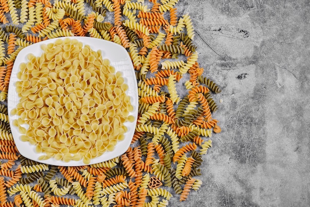 Photo gratuite fusilli colorés et bol de pâtes crues sur fond de marbre