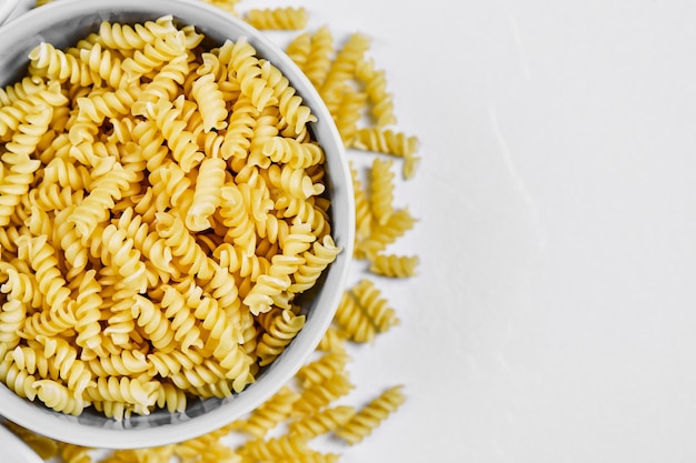 Fusilli cru et un bol de farine sur blanc.