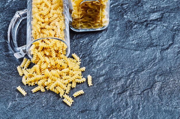 Fusilli cru à l'extérieur d'un bocal en verre sur bleu.