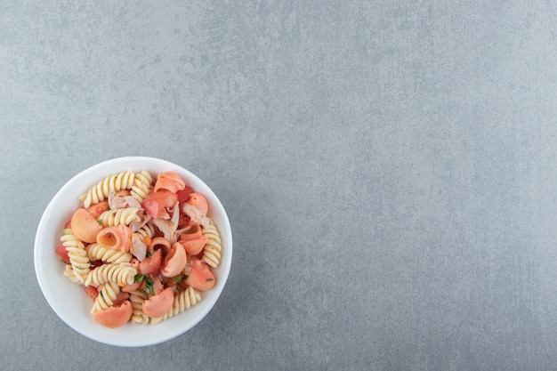 Fusilli et pâtes aux coquillages rouges dans un bol blanc.