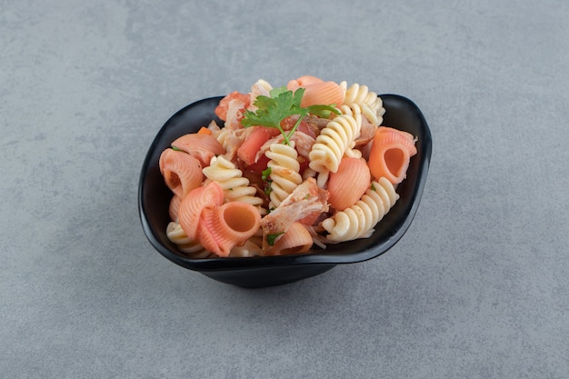 Fusilli et pâtes aux coquillages rouges dans un bol noir.