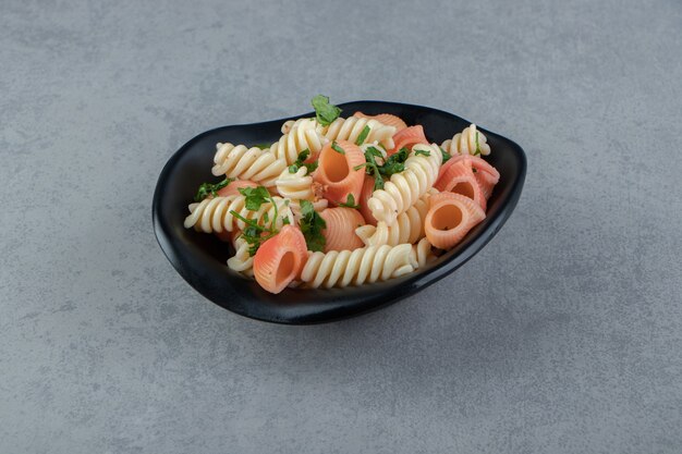 Fusilli et pâtes aux coquillages rouges dans un bol noir.