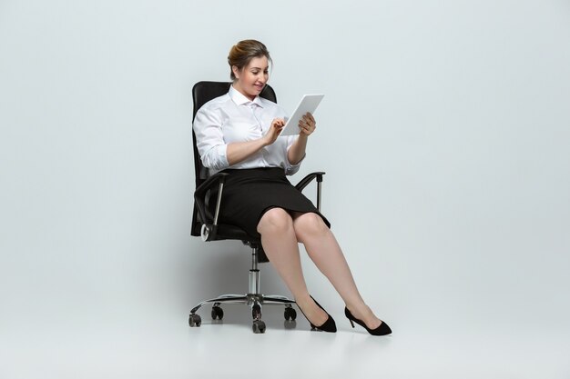 Gadgets. Jeune femme en tenue de bureau. Personnage féminin Bodypositive, féminisme, s'aimer, concept de beauté. Femme d'affaires de grande taille sur mur gris. Patron, magnifique. Inclusion, diversité.