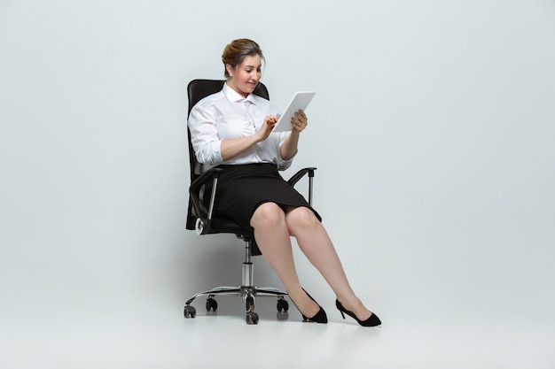 Gadgets. Jeune femme en tenue de bureau. Personnage féminin Bodypositive, féminisme, s'aimer, concept de beauté. Femme d'affaires de grande taille sur mur gris. Patron, magnifique. Inclusion, diversité.