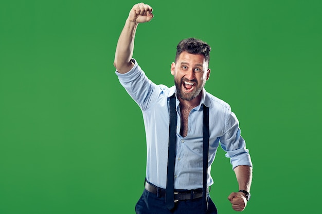 Gagner le succès homme heureux célébrant être un gagnant. Image dynamique du modèle masculin caucasien sur le mur vert. Victoire, concept de plaisir. Concept d'émotions faciales humaines.