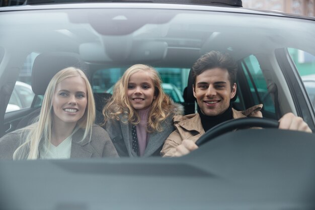 Gai homme assis dans la voiture avec sa femme et sa fille