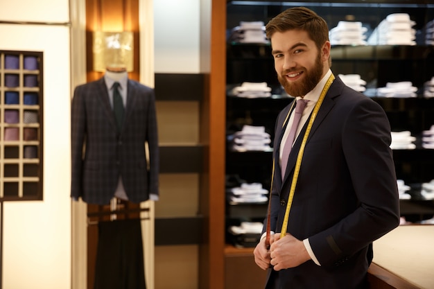 Gai homme barbu portant un costume bleu debout avec du ruban à mesurer dans l'armoire