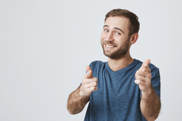 Gai homme barbu vous félicite, pointant l'appareil photo du doigt