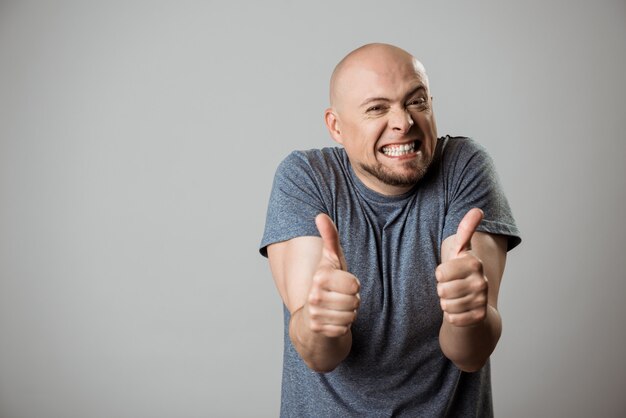 Gai jeune homme souriant, montrant bien sur mur beige