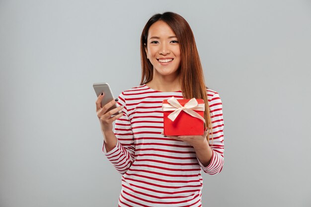 Gaie jeune femme asiatique bavardant par téléphone tenant le cadeau.