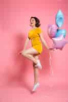 Photo gratuite gaie jeune femme en robe jaune tenant des ballons