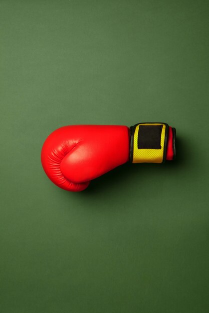 Gant de boxe rouge et jaune vif. Équipement de sport professionnel isolé sur fond vert studio. Concept de sport, activité, mouvement, mode de vie sain, bien-être. Couleurs modernes.