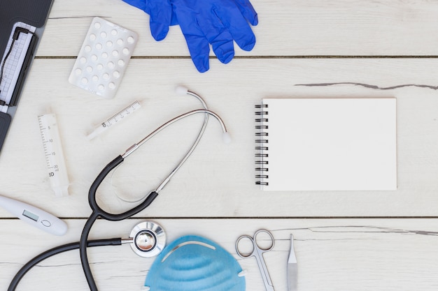 Gants; des pilules; bloc-notes à spirale et équipement médical sur un bureau en bois blanc