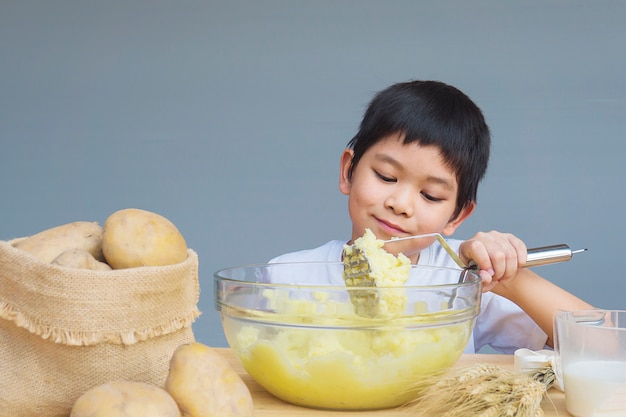 Garçon de 7 ans préparant une purée de pommes de terre avec joie
