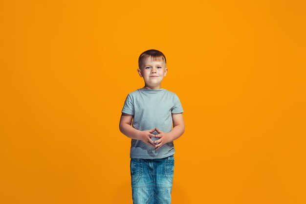 Le garçon adolescent heureux debout et souriant contre l'espace orange.