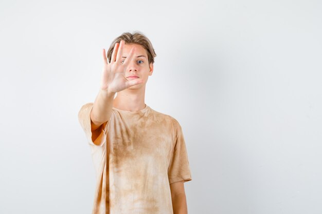 Garçon adolescent mignon montrant un geste d'arrêt en t-shirt et ayant l'air sérieux. vue de face.