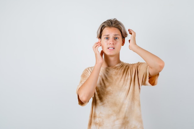 Garçon adolescent en t-shirt gardant les mains près de la tête et ayant l'air troublé, vue de face.