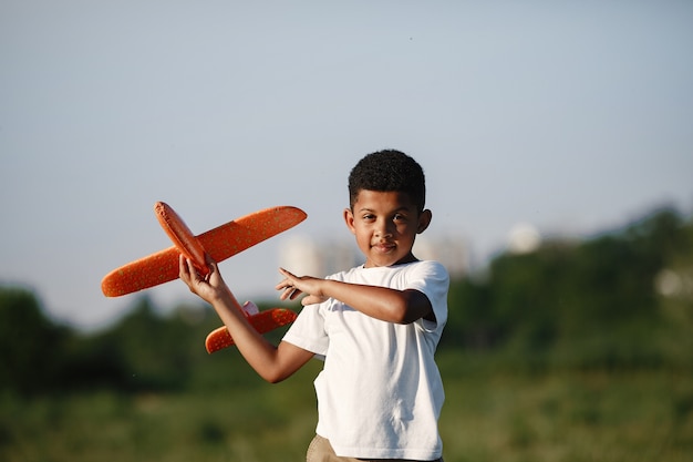 Photo gratuite garçon africain détient jouet avion jouant seul. enfant dans un parc d'été.