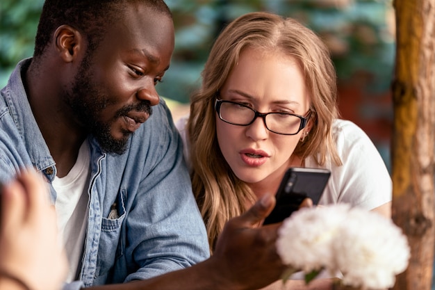 Garçon africain montre smartphone choquant sur le smartphone à belle femme de race blanche