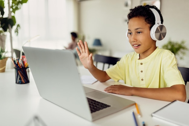 Photo gratuite garçon afro-américain utilisant un ordinateur portable et agitant pendant un appel vidéo pendant l'enseignement à domicile