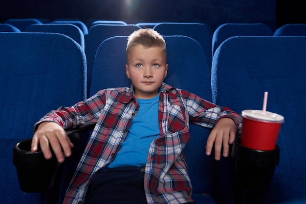 Garçon assis au cinéma, regardant attentivement le film.