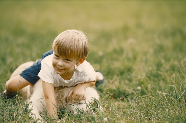 Garçon aux cheveux blonds jouant sur une herbe avec son chien. garçon portant un t-shirt blanc et un short bleu