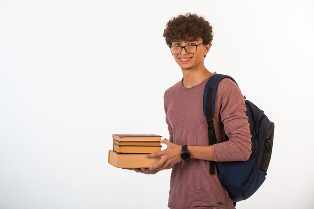 Garçon aux cheveux bouclés dans des lunettes optiques tenant des livres scolaires à deux mains et souriant.