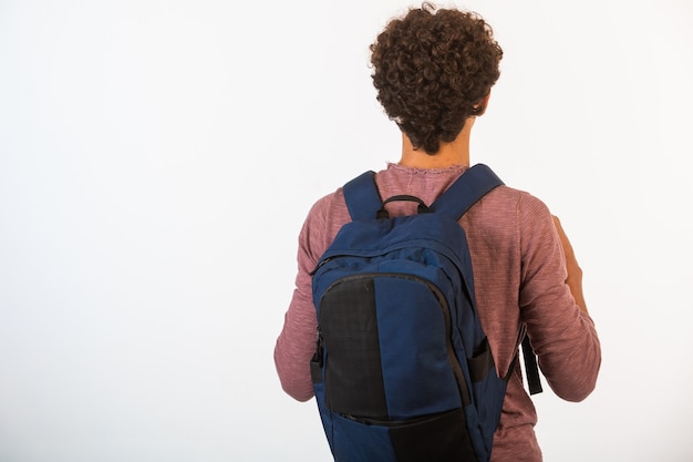 Garçon aux cheveux bouclés dans des lunettes optiques tenant son sac à dos, vue de derrière.