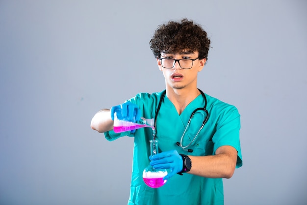 Garçon aux cheveux bouclés en uniforme médical et masques à main mettant un liquide rose d'un flacon à l'autre