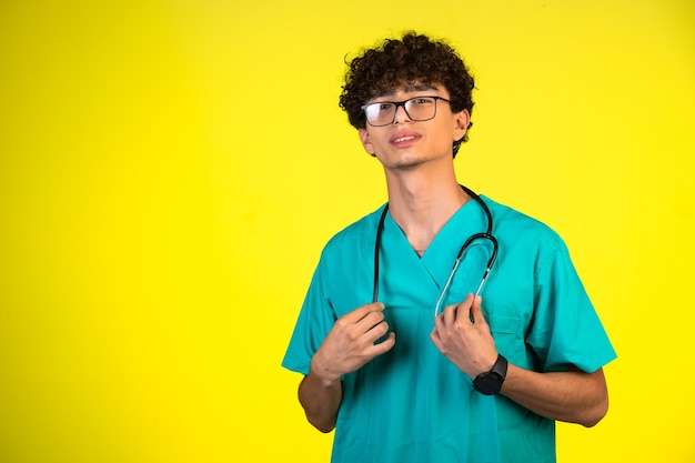 Garçon aux cheveux bouclés en uniforme médical tenant son stéthoscope.