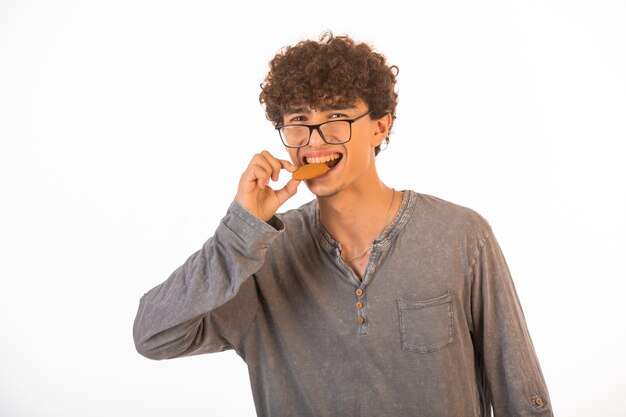 Garçon aux cheveux bouclés et verres optiques dégustant un biscuit.