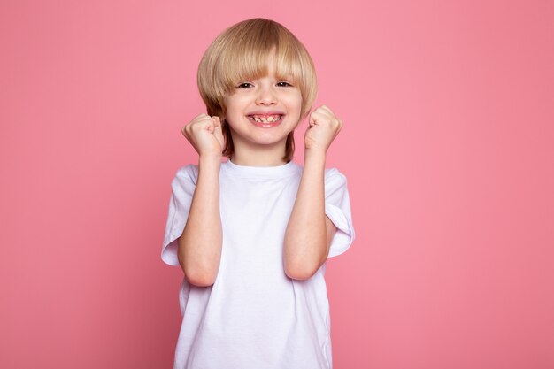 Garçon blond adorable mignon souriant en t-shirt blanc sur rose