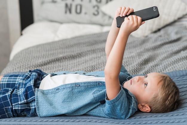 Garçon blond allongé sur le lit à l&#39;aide d&#39;un téléphone portable