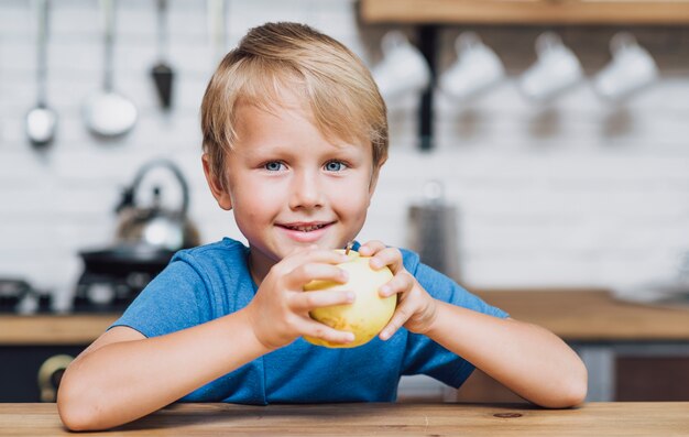 Garçon blond vue de face mange une pomme