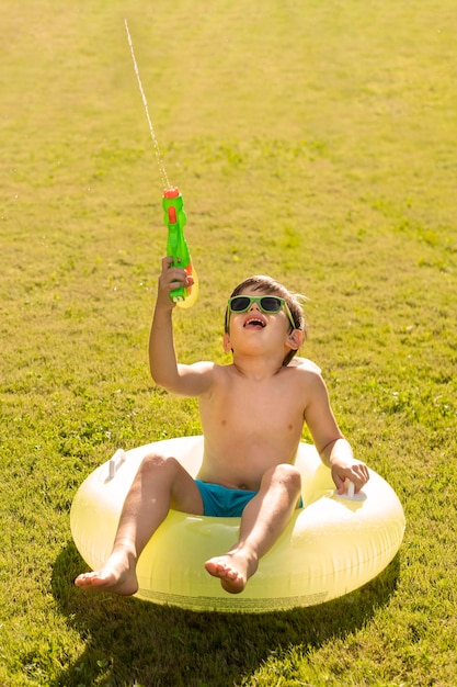 Garçon avec chapeau et lunettes de soleil jouant avec pistolet à eau