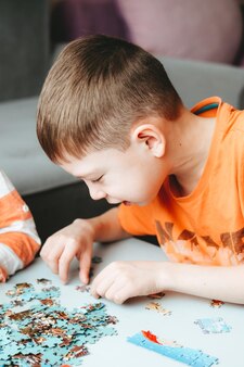Le garçon dans un t-shirt orange rassemble un puzzle sur la table temps sans gadgets. jeux de société pour les enfants. le garçon développe la motricité fine et le cerveau