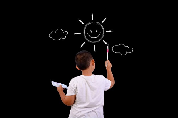 Un garçon dessine le ciel et le soleil avec un tableau noir