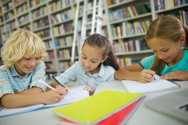 Garçon et deux filles écrivant à table