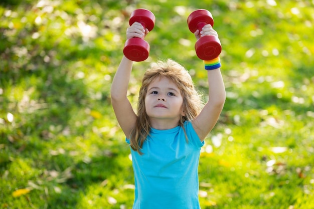 Garçon enfant en bonne santé avec exercice d'haltères en plein air petit enfant pratique des exercices d'haltères dans le parc
