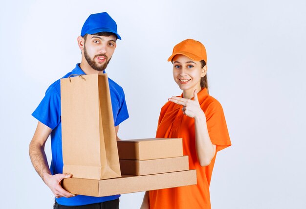 Photo gratuite garçon et fille de courrier en uniformes bleus et jaunes tenant des boîtes à emporter en carton et des colis commerciaux.