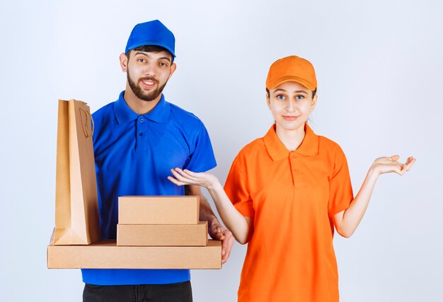 Garçon et fille de courrier en uniformes bleus et jaunes tenant des boîtes à emporter en carton et des colis commerciaux.