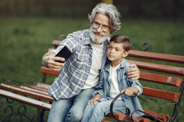 Garçon et grand-père assis sur un banc. Famille dans le parc. Vieil homme jouant avec son petit-fils. Grand-père utilise un téléphone.