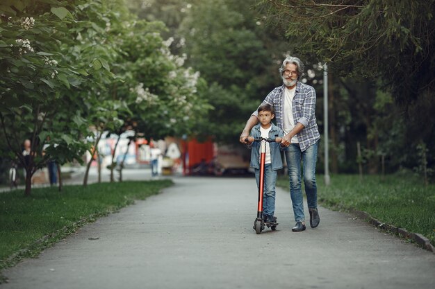 Garçon et grand-père marchent dans le parc. Vieil homme jouant avec son petit-fils. Enfant avec scooter.
