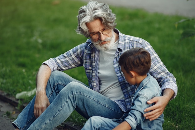 Garçon Et Grand-père Marchent Dans Le Parc. Vieil Homme Jouant Avec Son Petit-fils. Famille Assise Sur L'herbe.