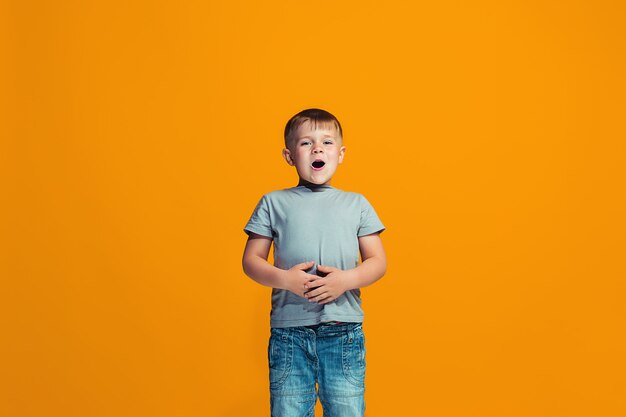 Le garçon heureux debout et souriant contre le mur orange