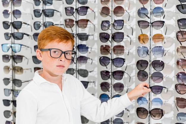 Garçon innocent regardant la caméra tenant un spectacle dans un magasin d'optique