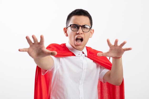 Garçon jeune super-héros insatisfait en cape rouge portant des lunettes regardant la caméra étirant les mains vers la caméra ne gesticulant pas isolé sur fond blanc